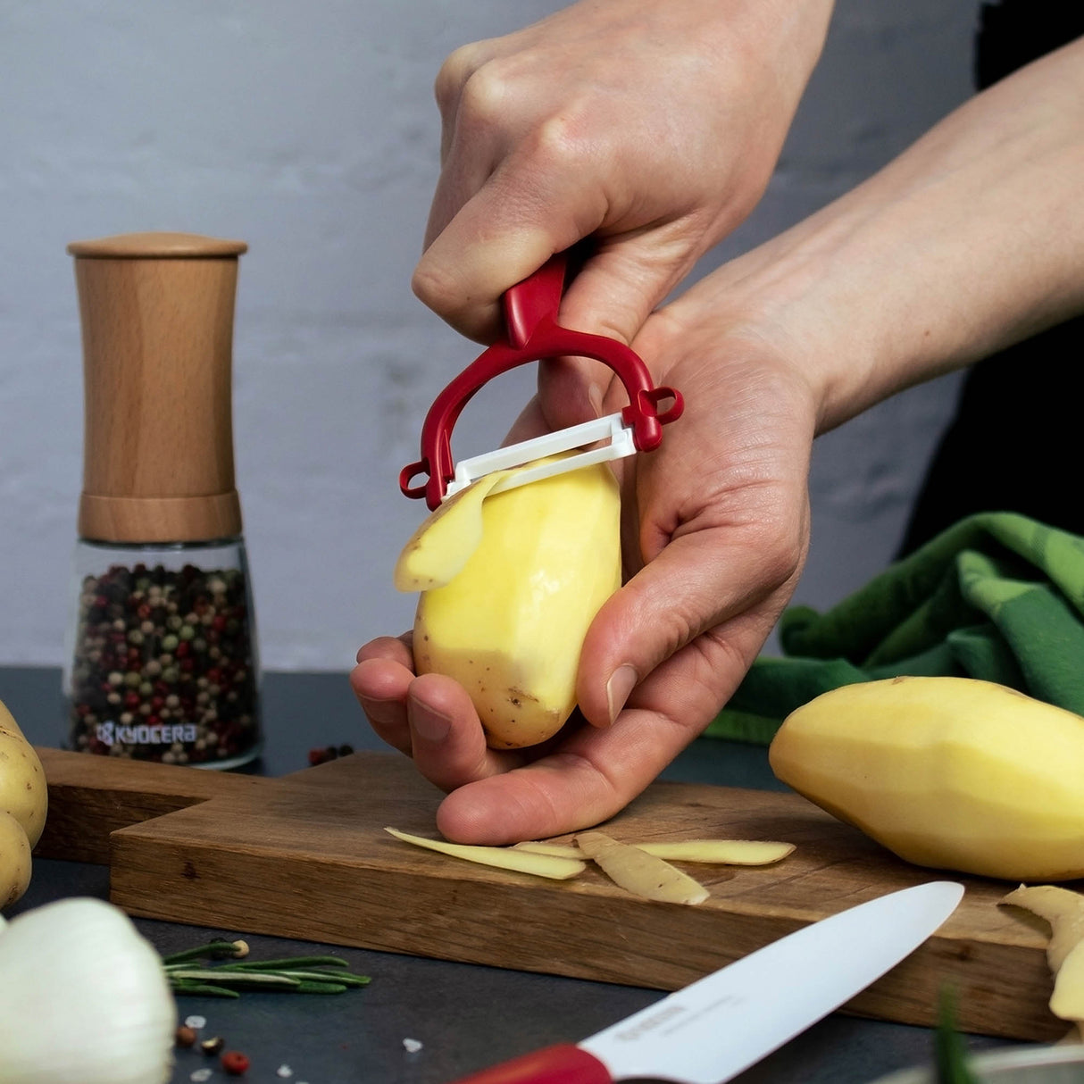 Grüner KYOCERA Schäler mit doppelseitigem Schliff, zeigt scharfe Klingen und ergonomisches Design für präzises Schneiden.