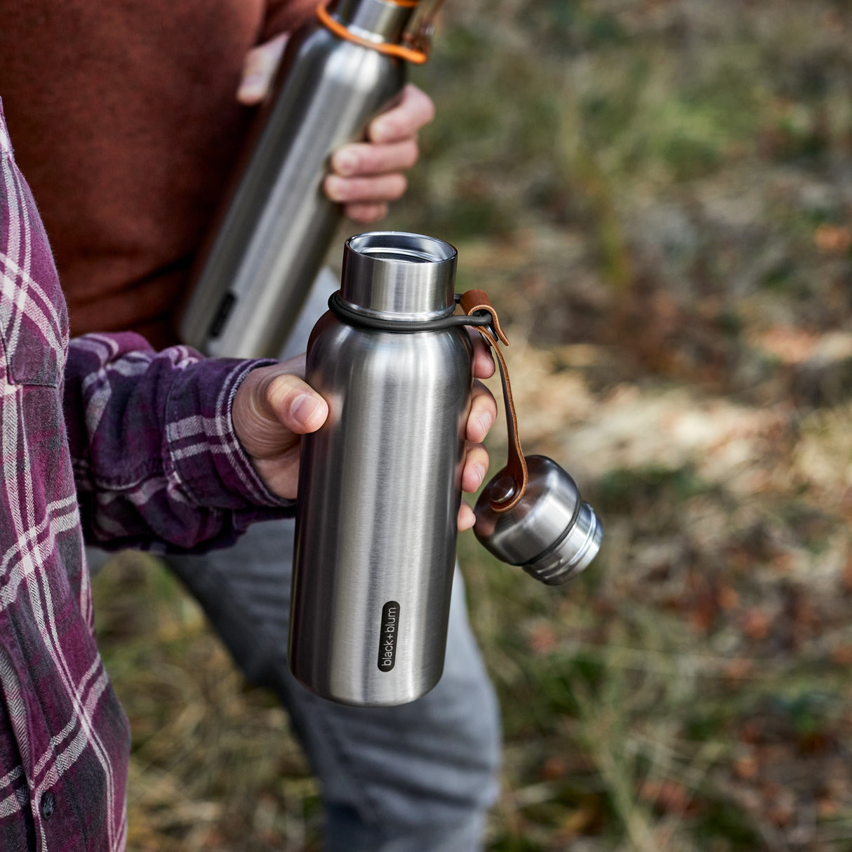 Schwarze BLACK+BLUM Isolierflasche aus Edelstahl, offen beim Wandern, ideal für heiße oder kalte Getränke unterwegs.