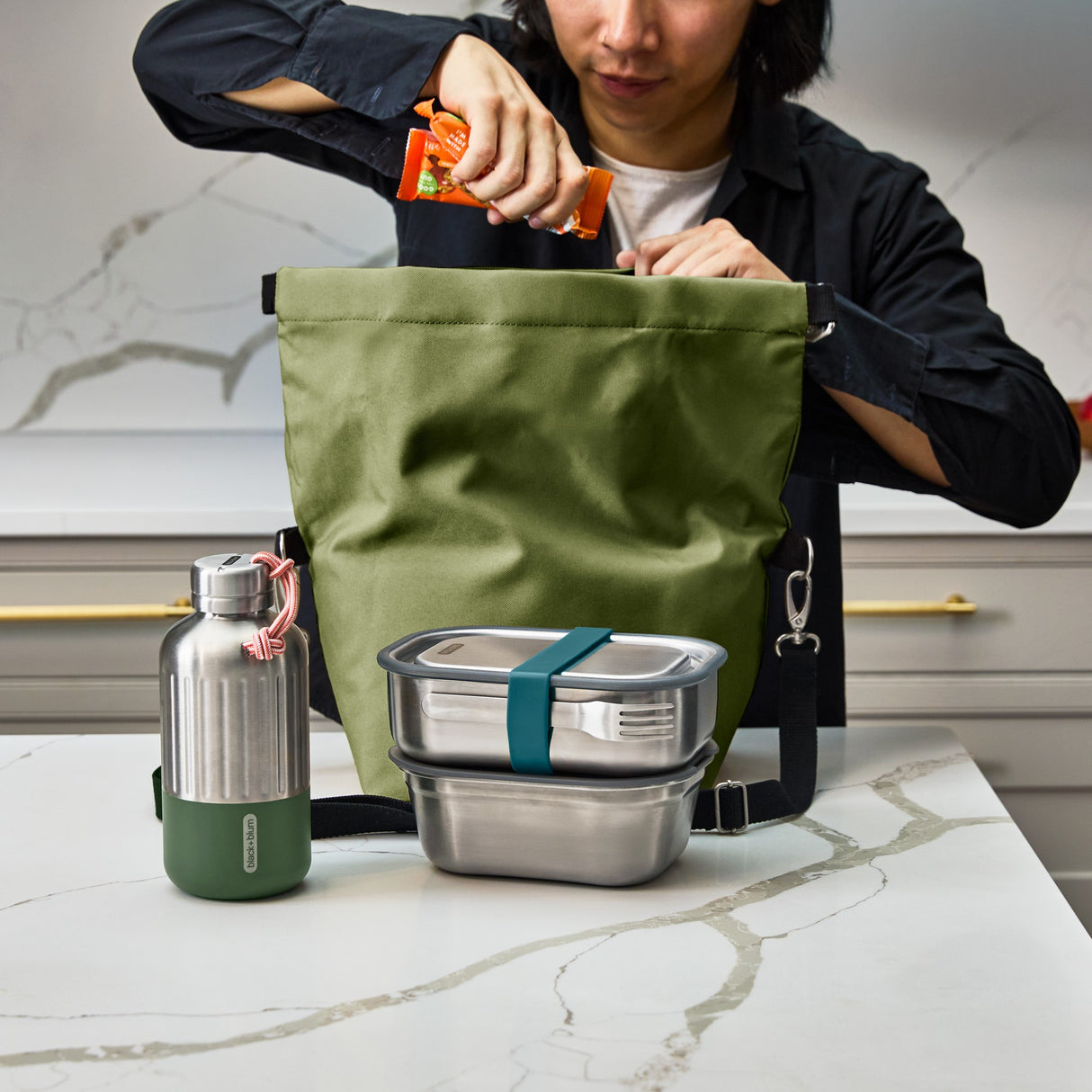 Schwarzer BLACK+BLUM Lunchbag, isoliert, offen auf einem Tisch mit Essen, für Lunch und unterwegs.