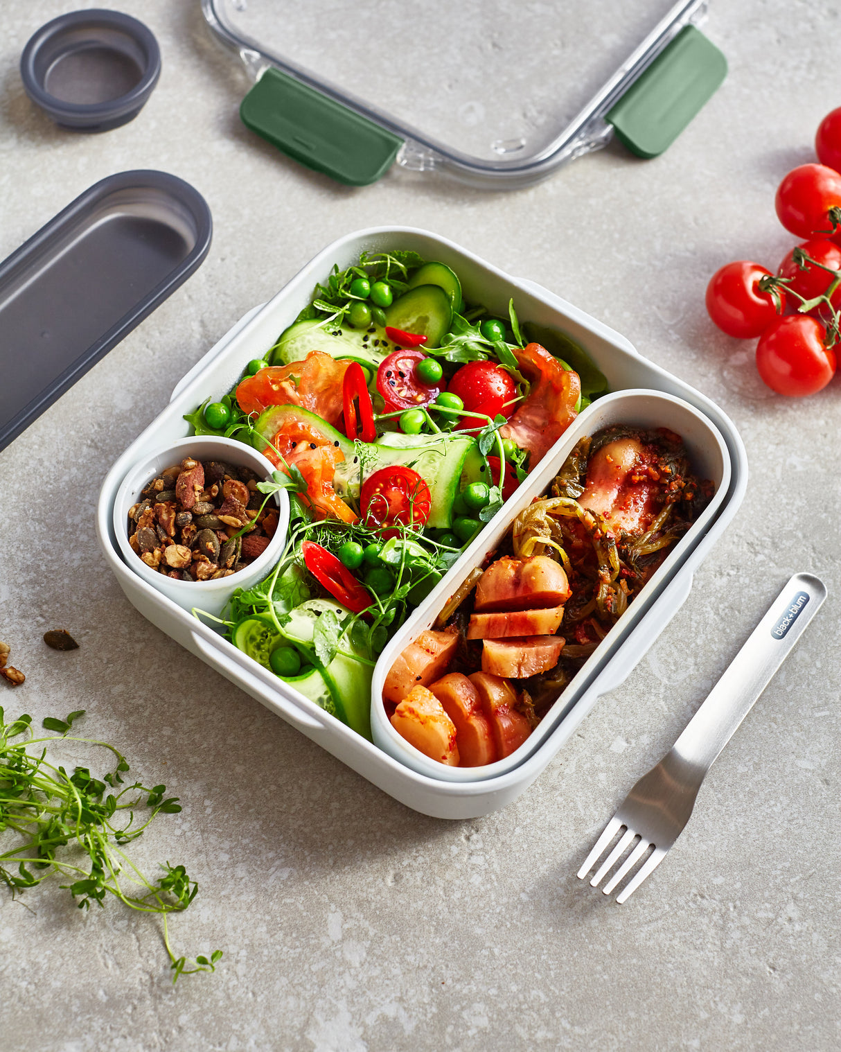 Schwarze BLACK+BLUM Lunchbox mit Salat und Oliven, langlebiges und stilvolles Behältnis für unterwegs.