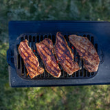 Schwarzer LODGE Grill aus Metall mit runder Kochfläche und klappbaren Griffen, ideal für Grillabende im Freien