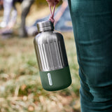 Schwarze BLACK+BLUM Explorer Isolierflasche aus Edelstahl, 650 ml, mit orangefarbenem Deckel und Oliv-Paracord.
