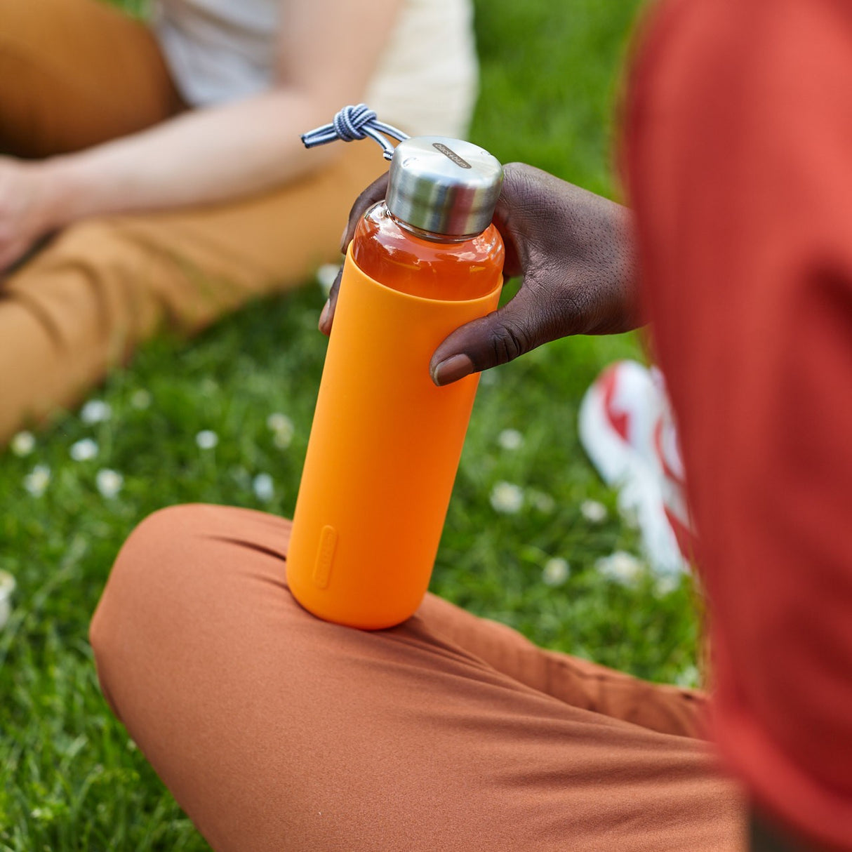 Schwarze BLACK+BLUM Trinkflasche aus Glas mit orangefarbenem Verschluss, 600 ml, ideal für unterwegs, langlebiges Design.