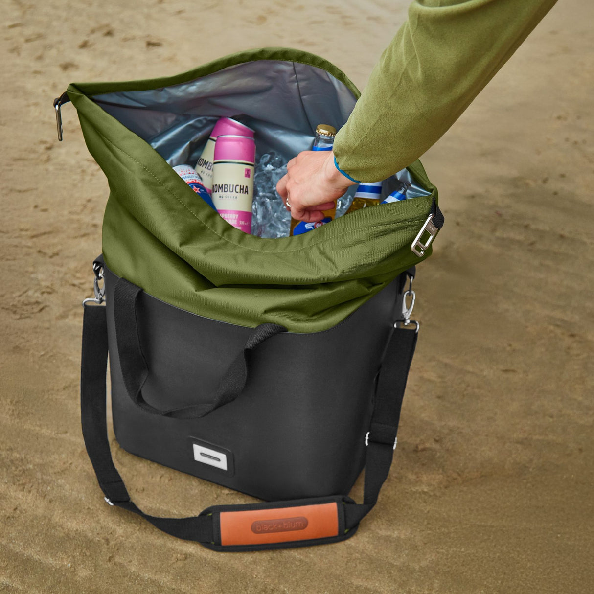 Faltbare, schwarze Kühlbox von BLACK+BLUM mit isolierter Innenausstattung, offen auf einem Strand.