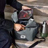 Schwarzer isolierter Lunchbag von BLACK+BLUM mit 10-Liter Fassungsvermögen, sitzend auf Treppen, vertikale Ansicht.